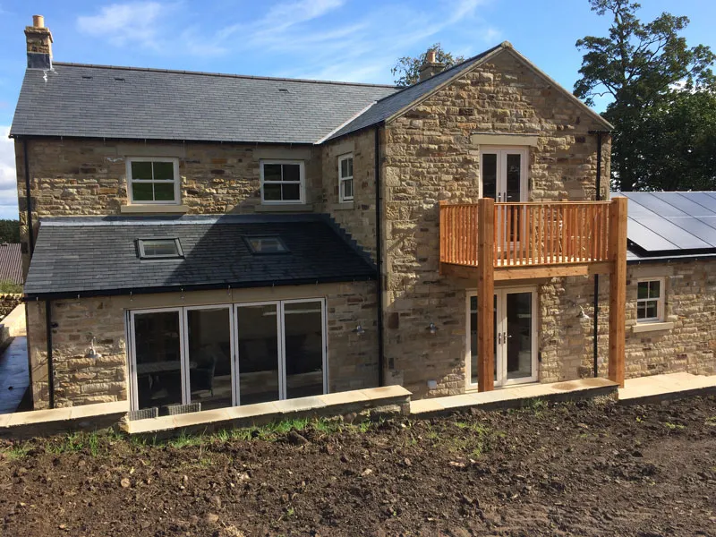 Stone house with large ground floor glazing and a timber balcony