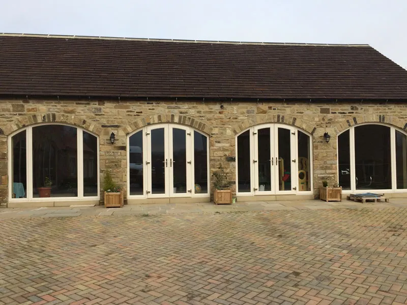 Stone barn conversion with arched glazed doors facing a block paved courtyard