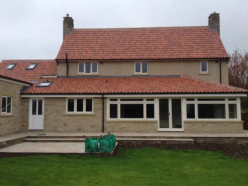 Rear of a stone house with white windows and patio doors opening onto a lawn