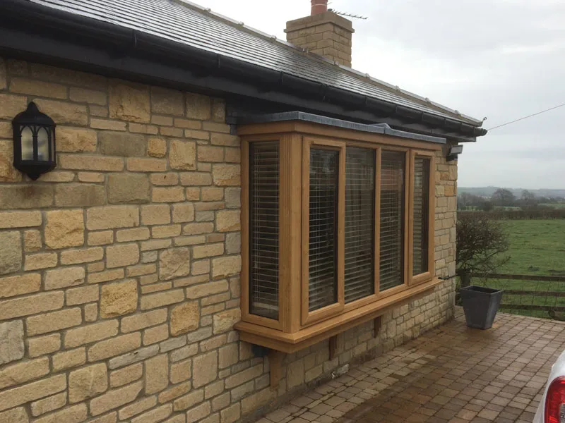 Oak woodgrain box bay window with shutters on a stone bungalow