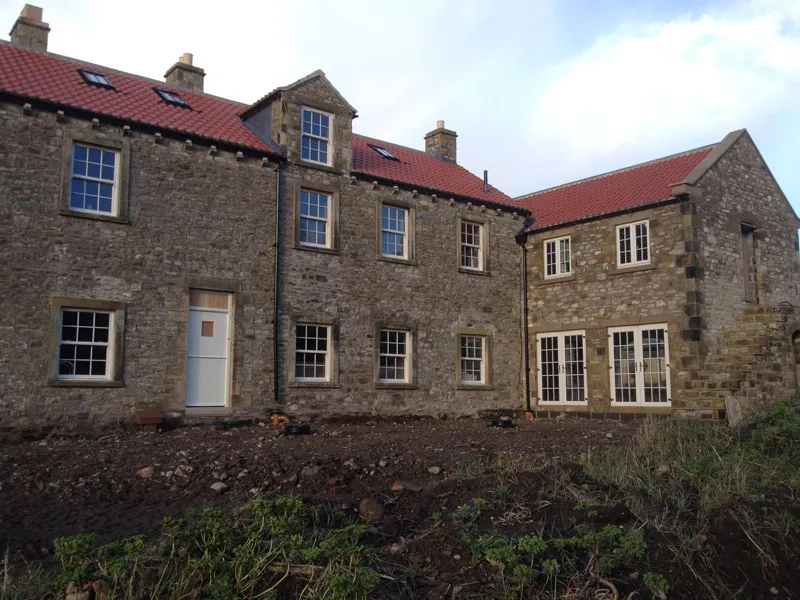 Row of stone farmhouses with white windows and doors under a red pantile roof
