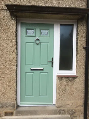Sage green composite front door with a glazed side panel in a stone doorway