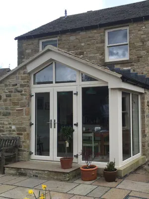 Gable-fronted conservatory with white French doors on a stone house