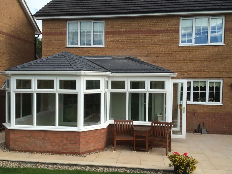 White Victorian-style conservatory with a tiled roof on a brick house