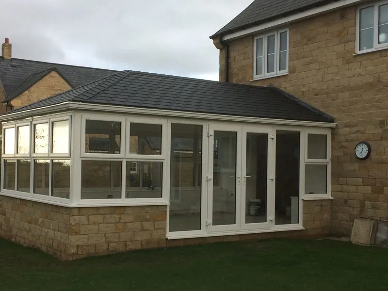 White conservatory with a tiled roof on a stone base