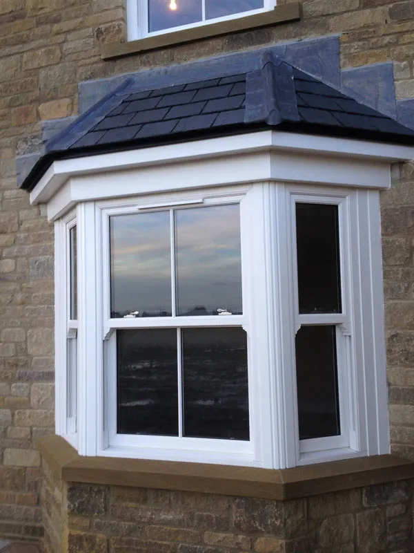 White bay window with a slate roof on a stone house