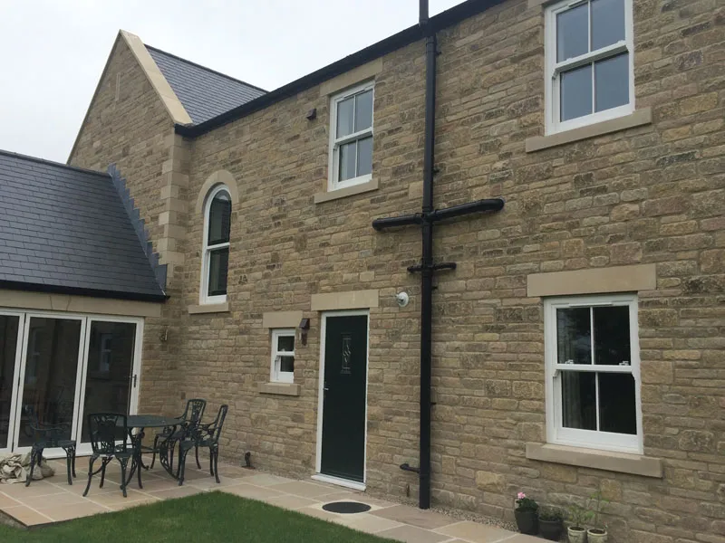 Stone house with white windows, an arched window and a dark green composite door